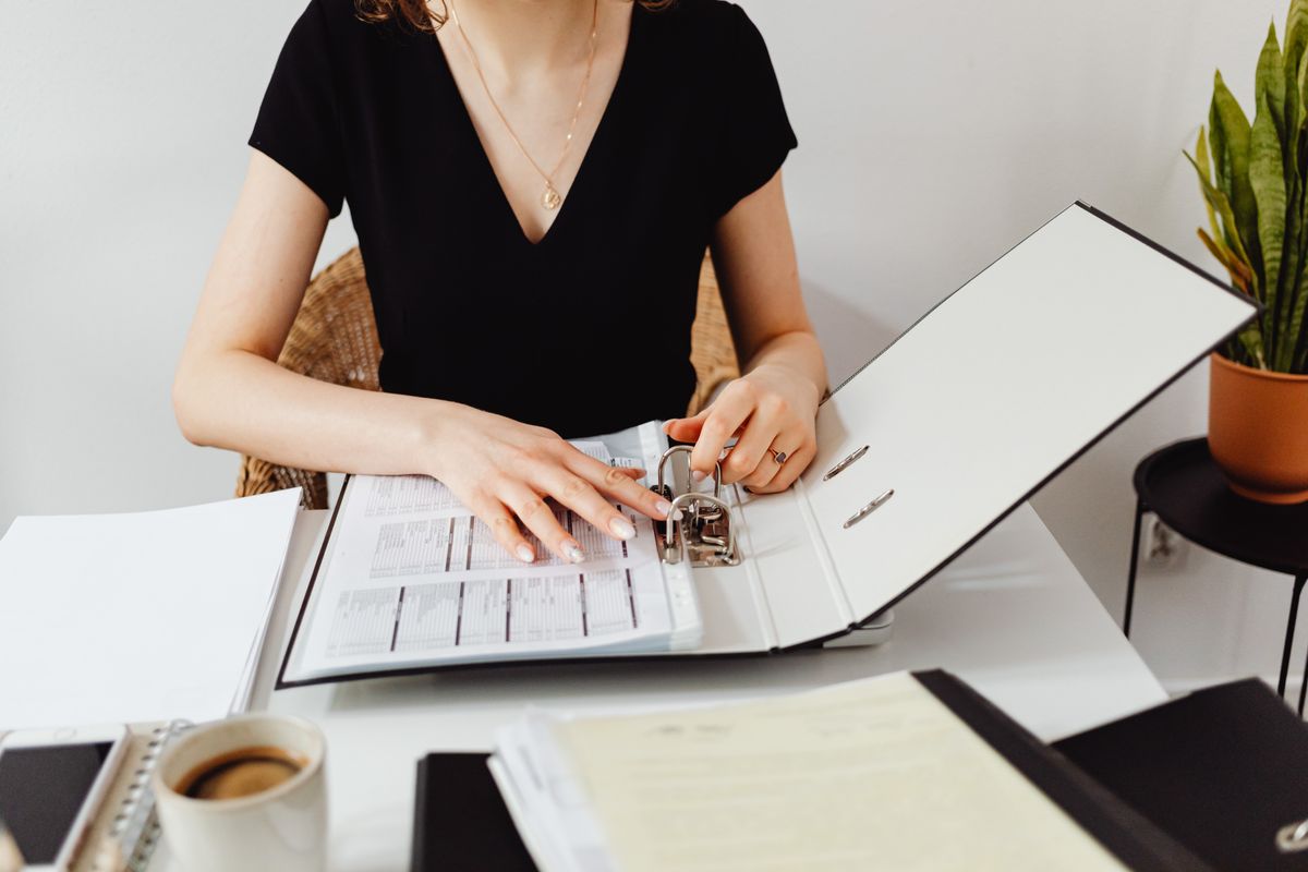 Femme qui range des documents dans un classeur à son bureau, une tasse de café à côté