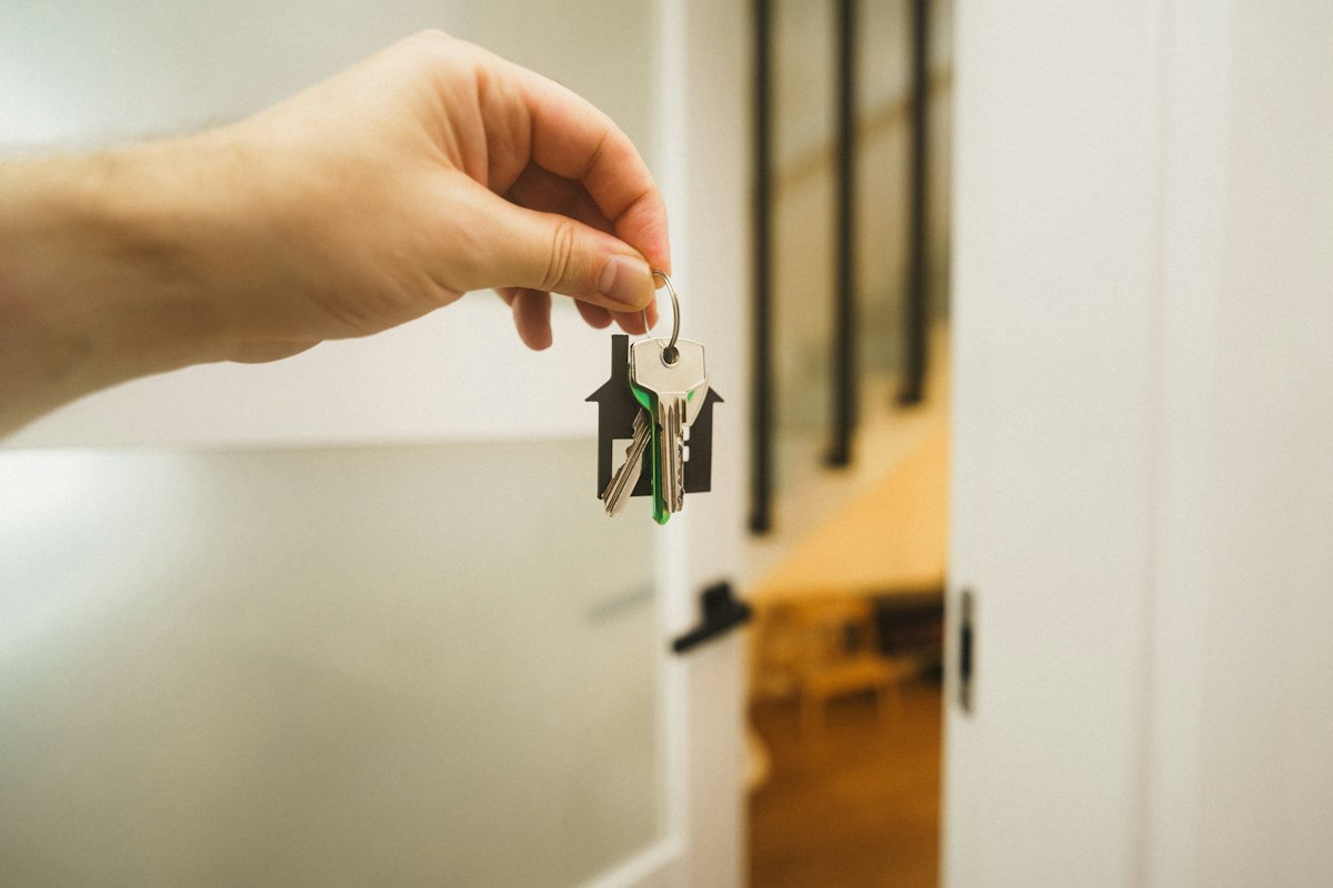 Main qui tend un trousseau de clés avec un porte-clés en forme de maison, devant une porte ouverte