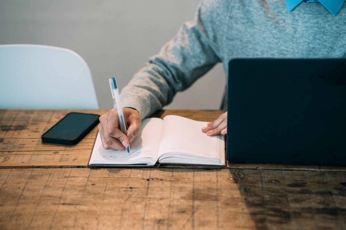 Main qui prend des notes dans un carnet à côté d'un ordinateur portable, sur une table en bois