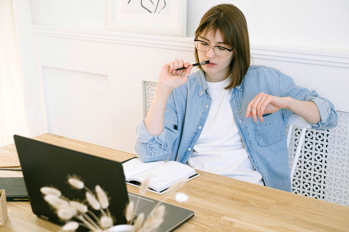 Femme pensive à son bureau à domicile, devant un ordinateur portable et un carnet