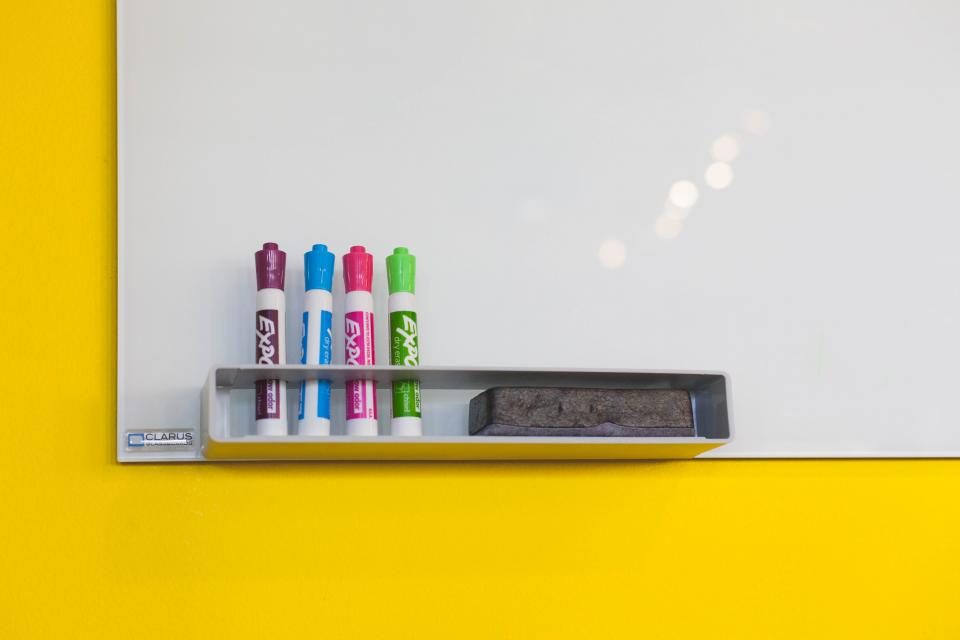 Tableau blanc vierge et quatre feutres de couleur sur un mur jaune