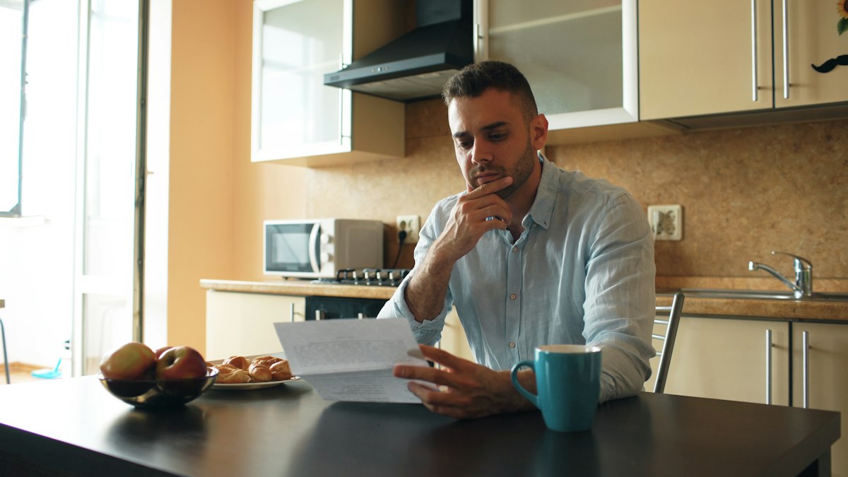 Homme soucieux qui lit un courrier à la table de sa cuisine